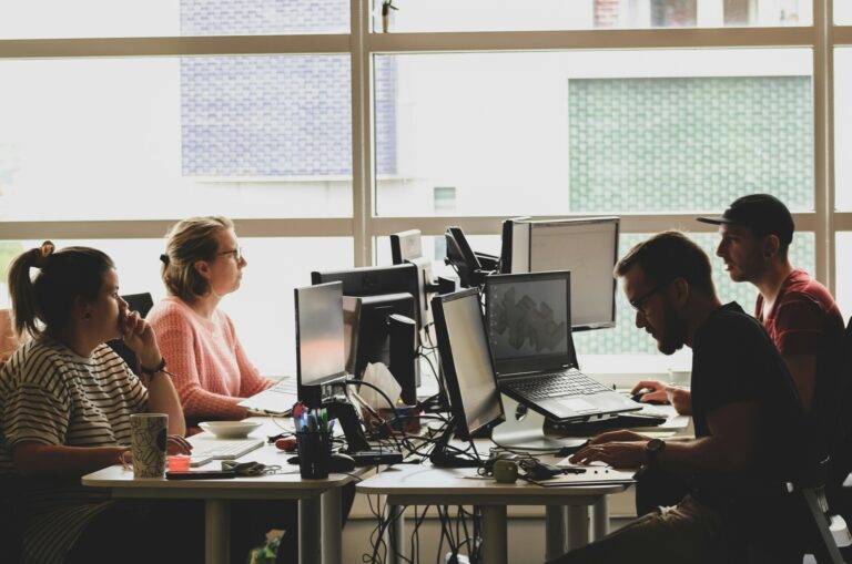 four people working at desks with computer screens